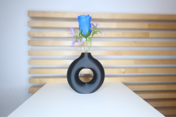 Jarrón Halo decorativo en color negro con diseño circular, colocado sobre una mesa con fondo de madera, ideal para aportar equilibrio y estilo a cualquier espacio